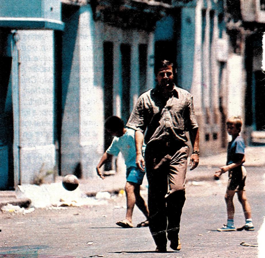 Imagen Una calle del Montevideo antiguo, cerca del puerto. Detrás un grupo, de botijas juega al fútbol sin pensar en el hombre que camina. 
